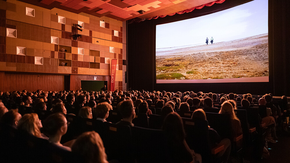 Saal mit großer Leinwand während ein Film mit zwei Fahrradfahrern läuft